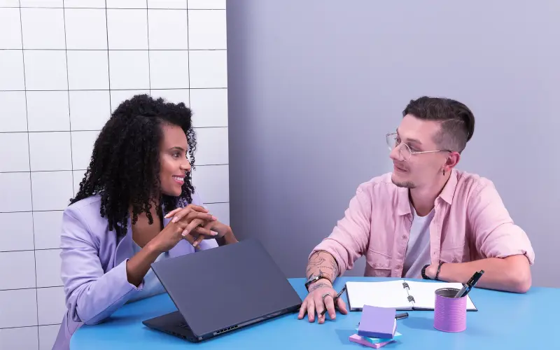 Imagem de uma mulher e um homem conversando em uma mesa de reunião.