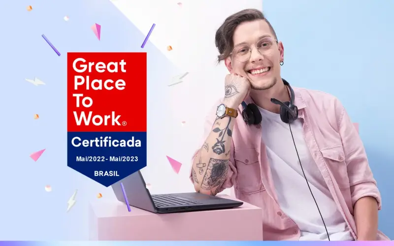 Imagem de um homem sorrindo, encostado em seu notebook. Ao fundo, o logo da Metadados, e ao seu lado, o selo de certificação Great Place to Work 2022