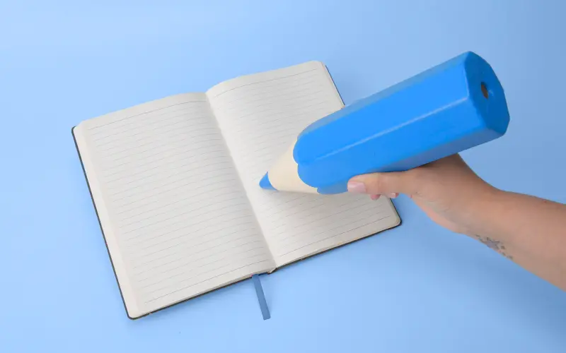 Imagem de um lápis gigante azul escrevendo em um caderno