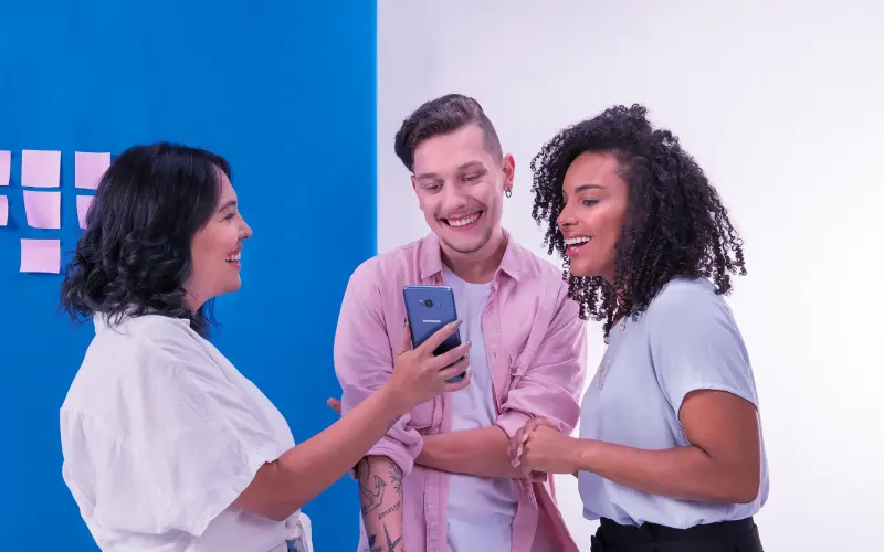 Imagem de uma mulher mostrando o celular para outras duas pessoas.