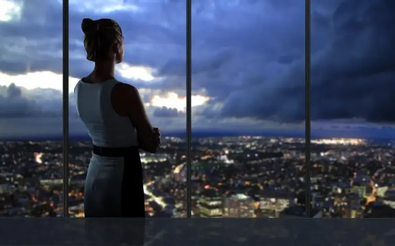 Imagem de uma mulher olhando paisagem de uma cidade pela janela à noite