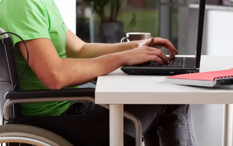 Imagem de um homem cadeirante em frente a uma mesa mexendo em um notebook