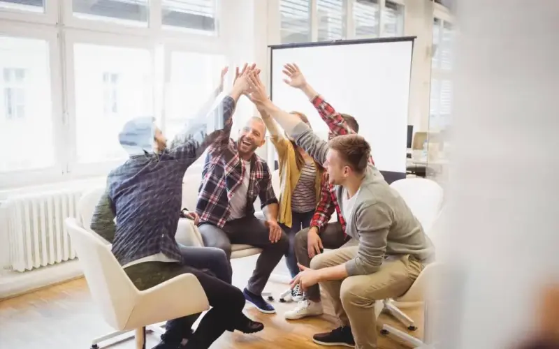 Imagem de um  time de pessoas comemorando em uma sala de reunião