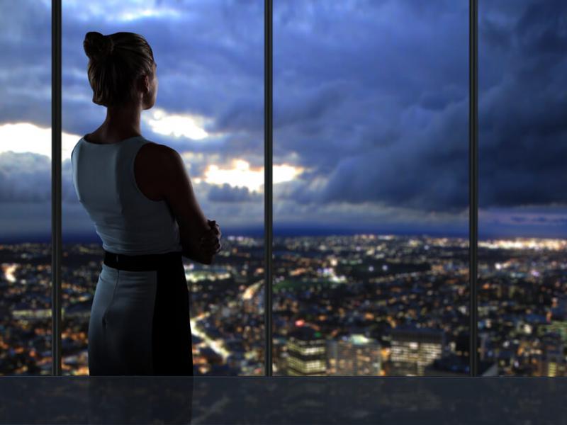 Imagem de uma mulher olhando paisagem de uma cidade pela janela à noite