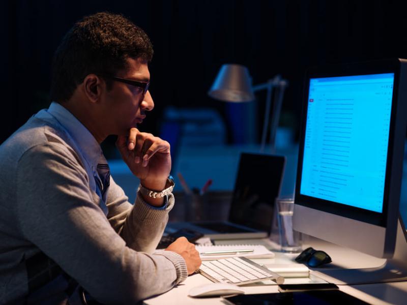 Foto de um homem trabalhando em frente a um computador à noite