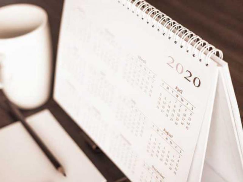 Imagem de um calendário, um bloco de anotações com um lápis e uma xícara de café