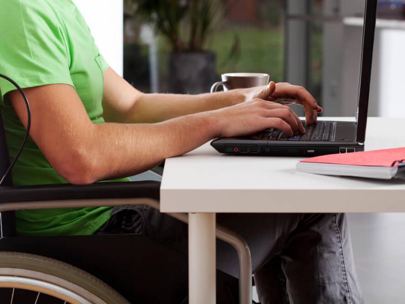 Imagem de um homem cadeirante em frente a uma mesa mexendo em um notebook
